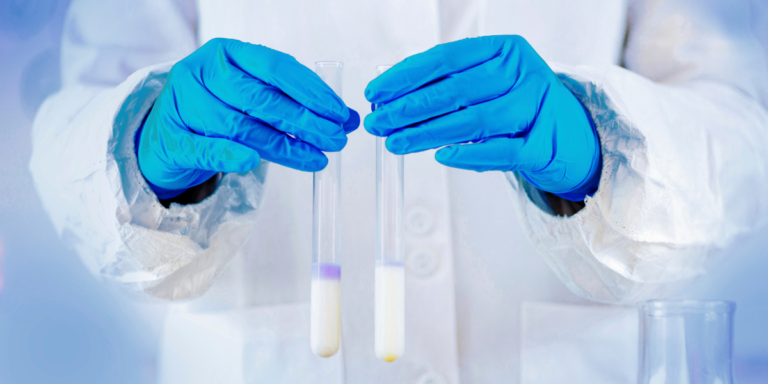 A person in a lab coat holds two test tubes, symbolizing pharmaceutical quality assurance and control in a lab setting.