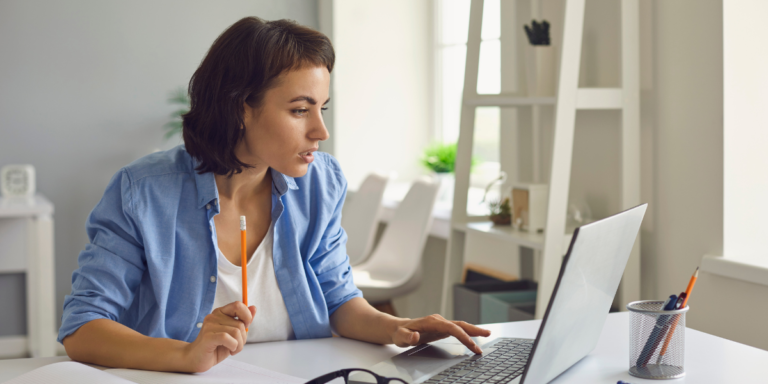 A woman sits at a desk with a laptop, focused on her studies in a healthcare course.