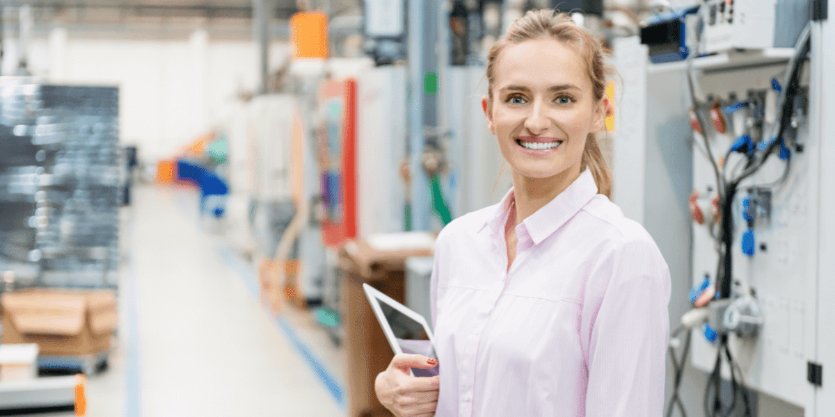 A woman in a factory holds a tablet, symbolizing her role in pharmaceutical quality control and career advancement opportunities.