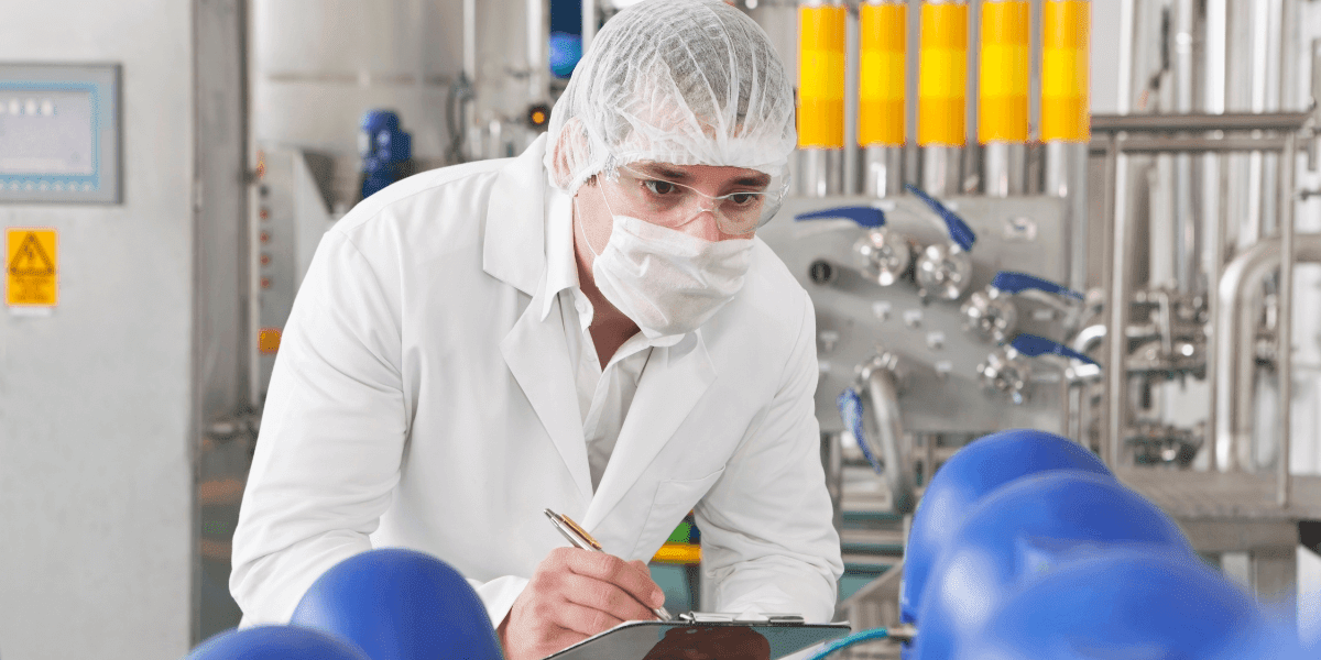 A man in a lab coat diligently writing on a clipboard, symbolizing quality control in pharmaceutical manufacturing.