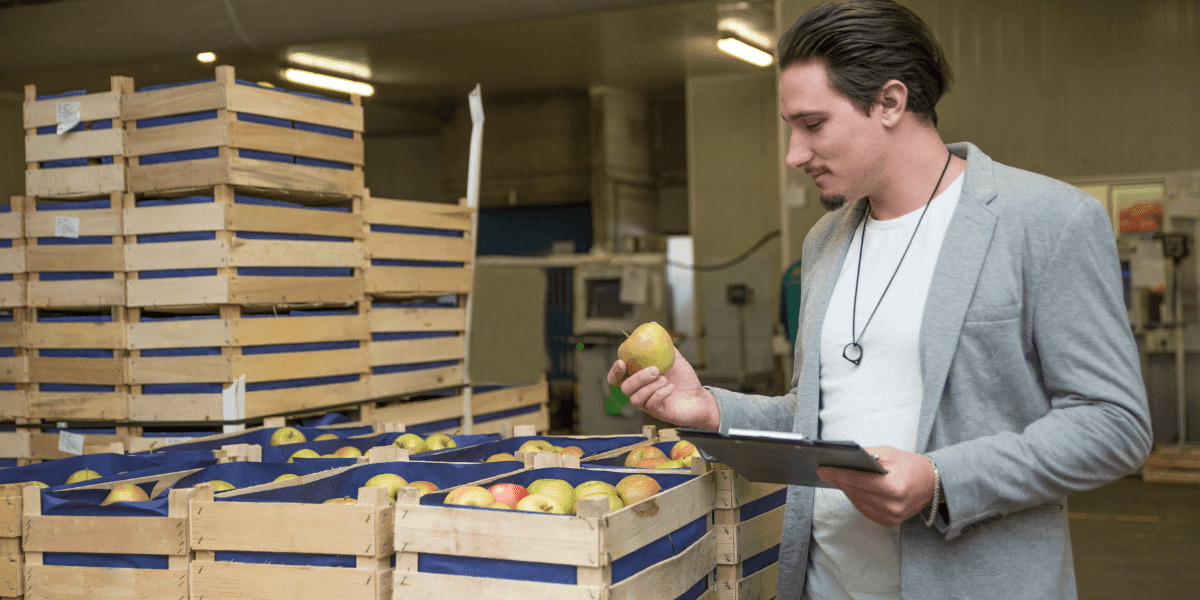 A man in a suit examines apples in crates, showcasing a moment of contemplation in a market setting.