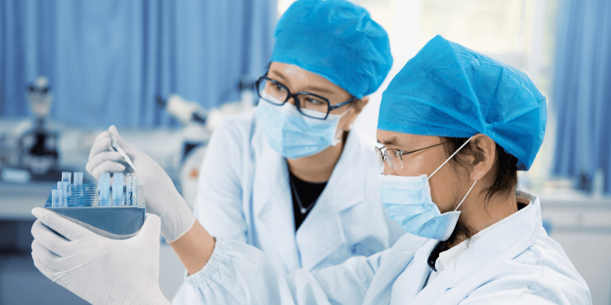 Two individuals in lab coats and masks collaborate on a project, emphasizing teamwork in pharmaceutical quality control.