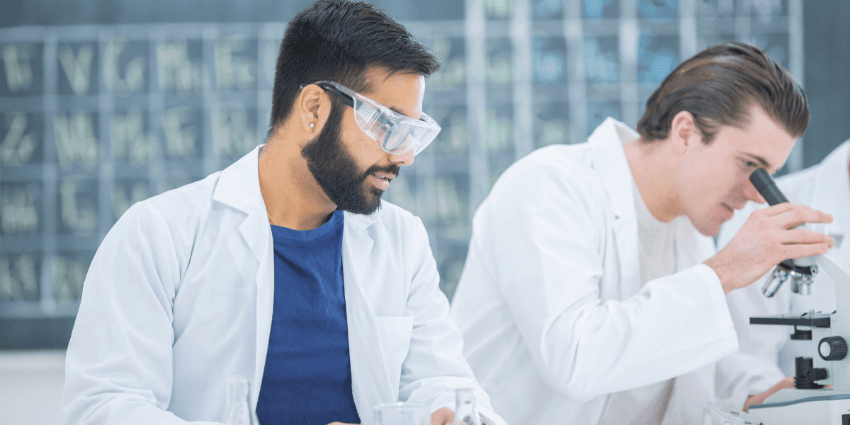 Two men in lab coats examining a microscope, symbolizing research and quality control in the pharmaceutical field.